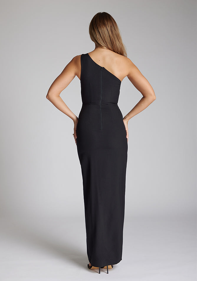 Back image of a brunette model wearing a monochrome dress in a maxi length with a asymmetric neckline, an ivory satin band across the neckline, thigh-high leg split and figure-hugging stretch crepe fabric with a white band across neckline. The design featured is the Vesper Fliss Monochrome Maxi Dress