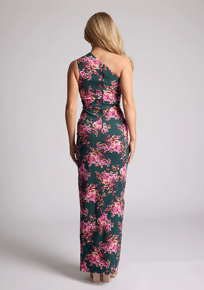 Back quarter image of a model wearing a green floral maxi dress with an asymmetric one-shoulder design, delicate pleats, and front skirt split. The design featured is the Vesper Charlotte Green Floral Maxi Dress.