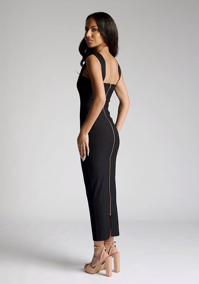 Back quarter image of a model wearing a black midaxi dress, featuring a scoop neckline with wide straps and a gold statement zip at the centre back. The dress feature is the Vesper Edina Black Midaxi Dress.