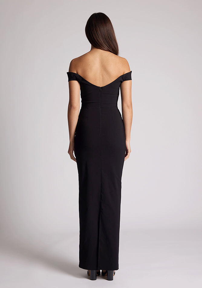 Back image of a model wearing a black maxi dress, featuring off-the-shoulder short sleeves and a dipped back design. The dress feature is the Vesper Holland Black Maxi Bardot Dress.