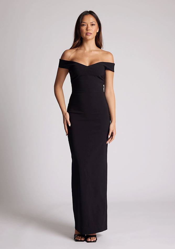 Front image of a model wearing a black maxi dress, featuring off-the-shoulder short sleeves and a dipped back design. The dress feature is the Vesper Holland Black Maxi Bardot Dress.
