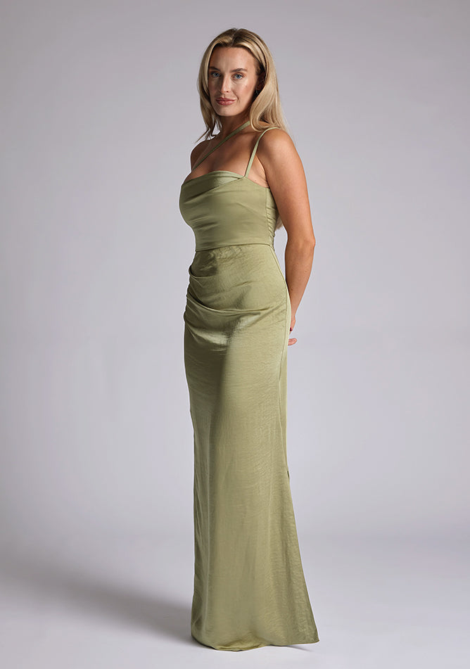 Front quarter image of a model wearing an olive satin maxi dress with a cross strap detail, pleats detailing at the front bust and delicate side skirt split. The design featured is the Vesper Solange Olive Satin Maxi Dress
