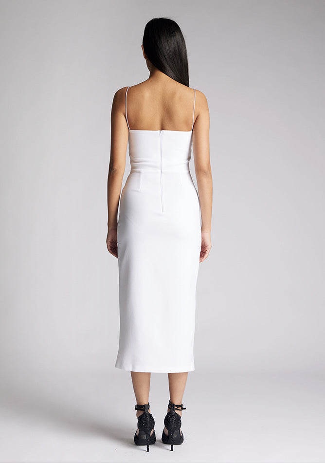 Back image of a model wearing a white midaxi dress with a minimalistic strap details, front skirt split and centre back zip. The design featured is the Vesper Tate White Midaxi Dress