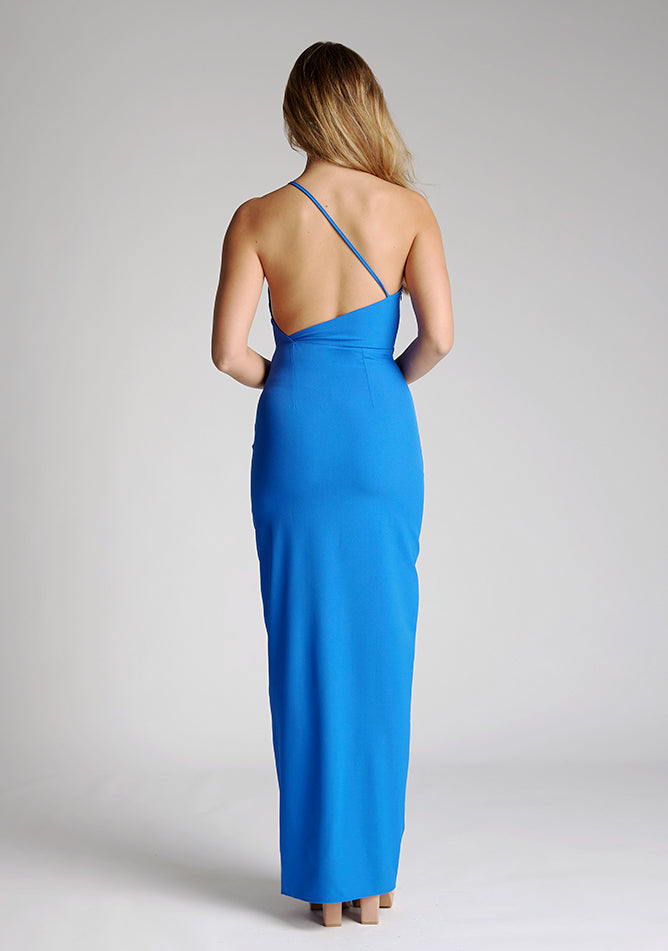 Back image of a model wearing a cobalt blue maxi dress with a asymmetric neckline, one shoulder strap, front skirt split and open back with asymmetric strap across back. The design featured is the Vesper Viva Cobalt One Shoulder Maxi Dress.