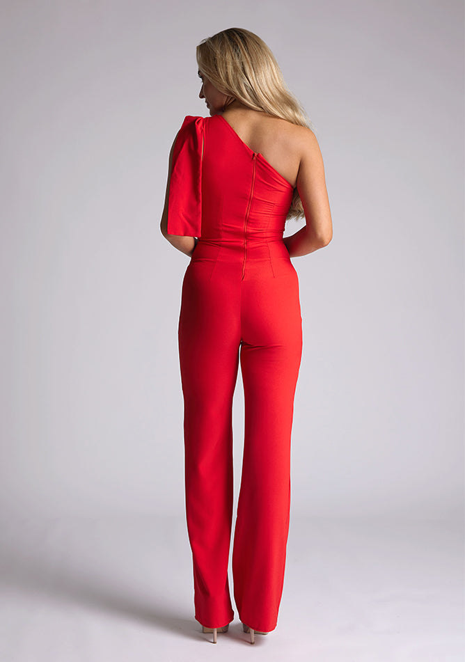 Back image of the model wearing a Red Jumpsuit with an asymmetric neckline and a bow on the shoulder. The design feature is the Vesper Gracie Red Jumpsuit.