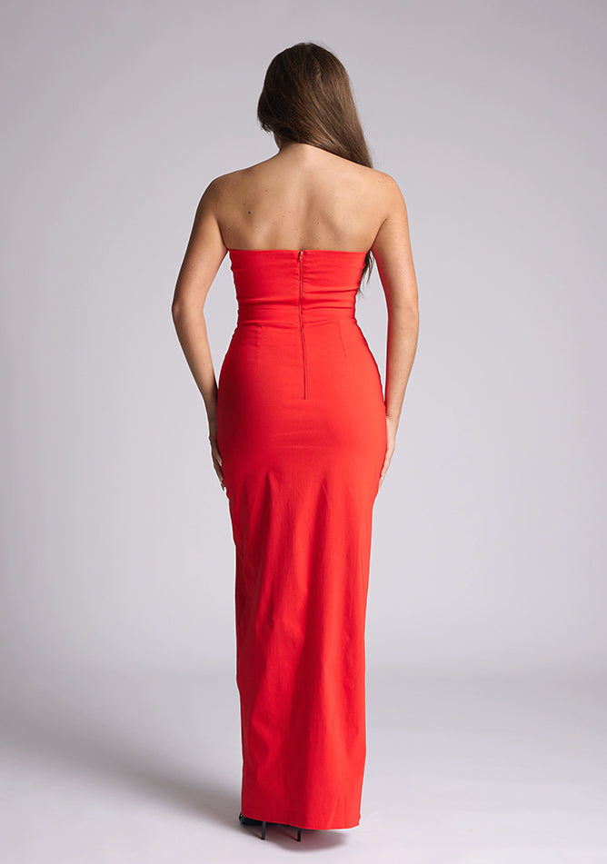 Back image of the model wearing a red bodycon maxi dress, with a strapless neckline and a front split. The design featured is the  Vesper Salma Red Midaxi Dress.