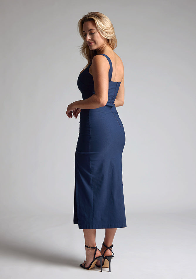 Back quarter image of the model wearing a navy bodycon midaxi dress with a square neckline with wide straps and a front skirt split. The design featured is the Vesper Abbie Navy Bodycon Midaxi Dress.