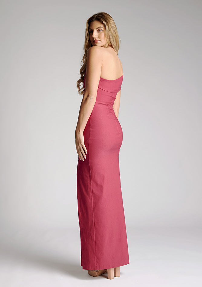 Back quarter image of model wearing a raspberry maxi dress with a stunning one-sleeve off-shoulder design and an alluring front skirt split. The design featured is the Vesper Carmel Raspberry Maxi Dress