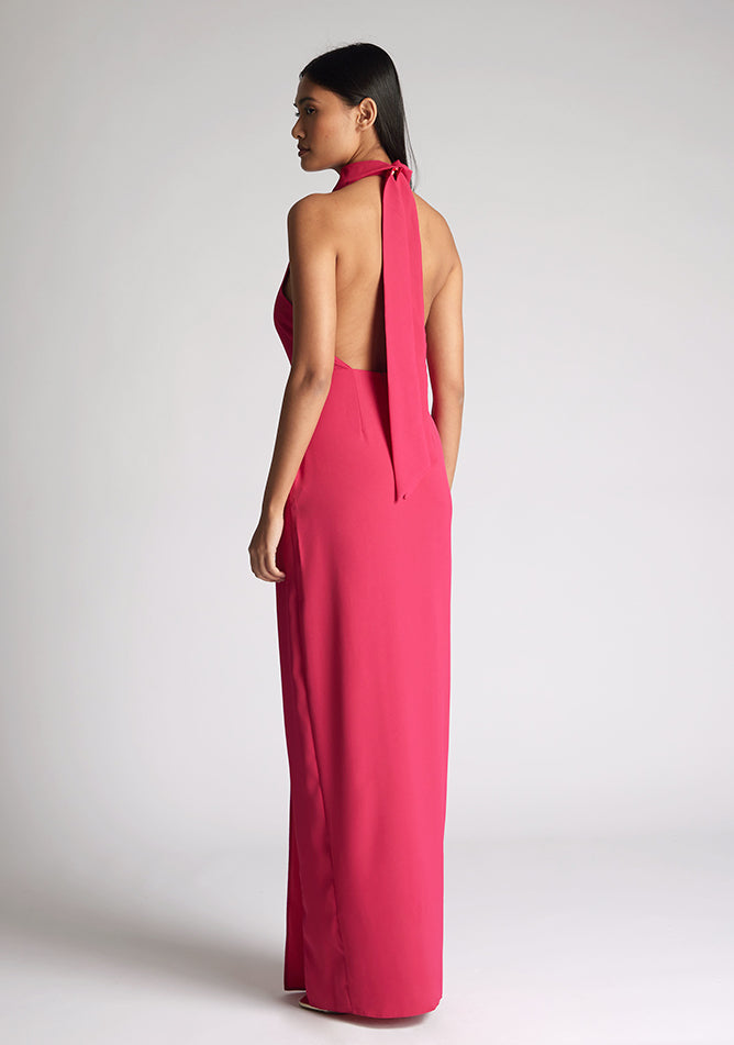 Back quarter image of a model wearing a cerise maxi dress with a flattering halter neckline and with its eye-catching blue hue and a front skirt split. The design featured is the Vesper Davina Cerise Maxi Dress