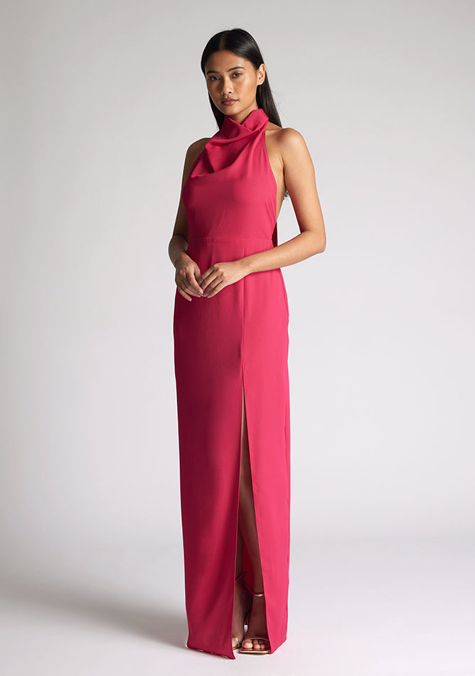 Front quarter image of a model wearing a cerise maxi dress with a flattering halter neckline and with its eye-catching blue hue and a front skirt split. The design featured is the Vesper Davina Cerise Maxi Dress