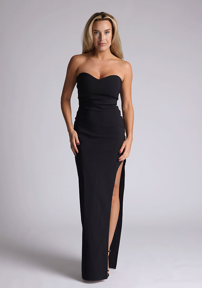 Front image of blonde model wearing a black maxi dress with a features a sweetheart neckline, centre back zip, and a side skirt split. The design featured is the Vesper Larissa Black Bodycon Maxi Dress