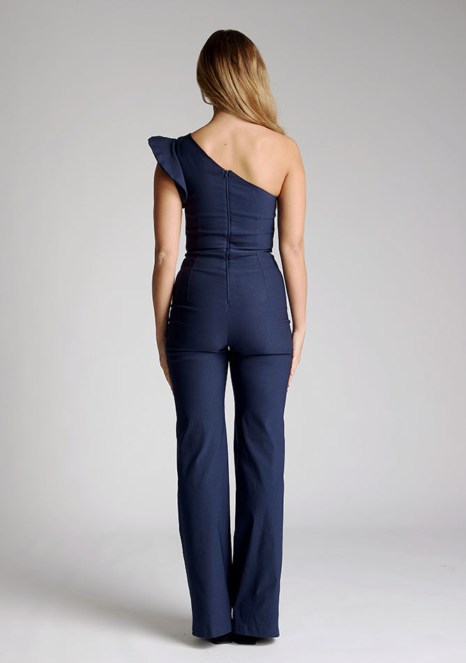 Back image of the model wearing a navy one shoulder jumpsuit
with a asymmetric neckline and one shoulder with a ruffle detail and wide leg finish elongates your silhouette, while the centre back zip ensures a sleek fit. The design featured is the Vesper Monty Navy One Shoulder Jumpsuit