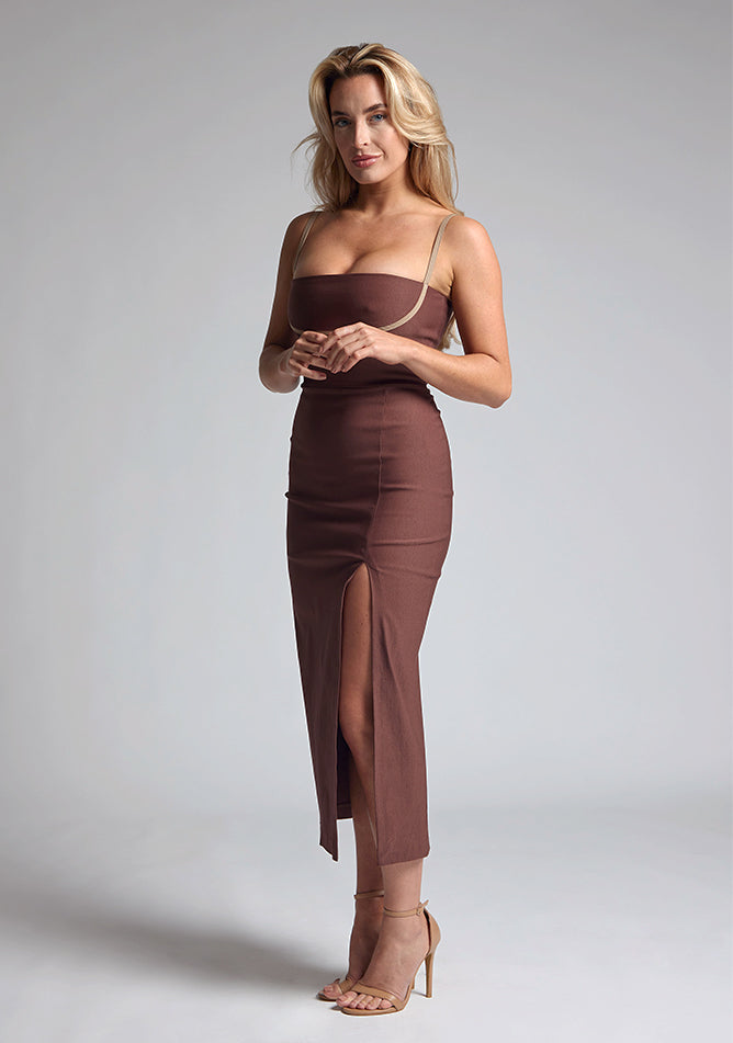 Front quarter image of a blonde model wearing a Chocolate Midaxi Dress with a daring plunge neckline, delicate thin straps, a flattering bodycon fit and a faux wrap skirt split adds a touch of sophistication to the overall design. The design features the Vesper Oaklynn Chocolate Midaxi Dress