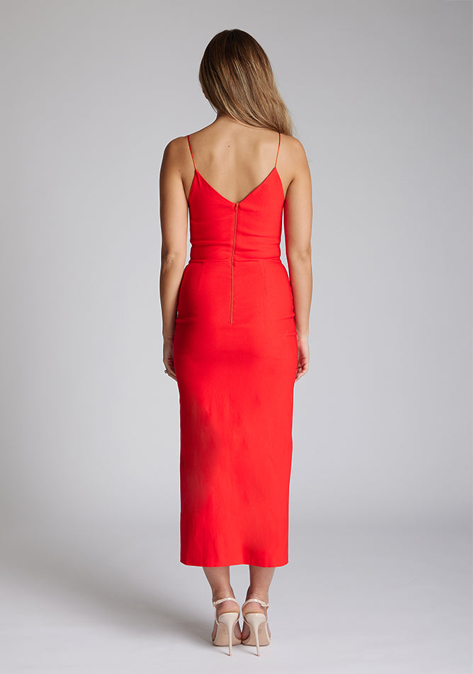 Back image of blonde model wearing a red midaxi dress with a plunge neckline, delicate thin straps for a feminine touch, and front split that adds a modern edge. The design featured is the Vesper Palmer Red Midaxi Dress