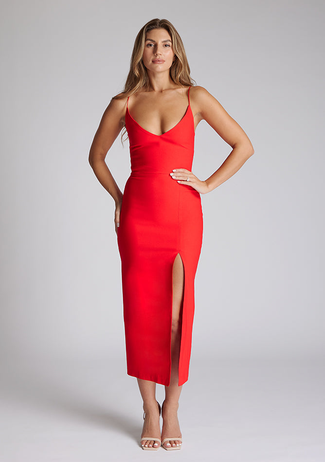 Front image of blonde model wearing a red midaxi dress with a plunge neckline, delicate thin straps for a feminine touch, and front split that adds a modern edge. The design featured is the Vesper Palmer Red Midaxi Dress