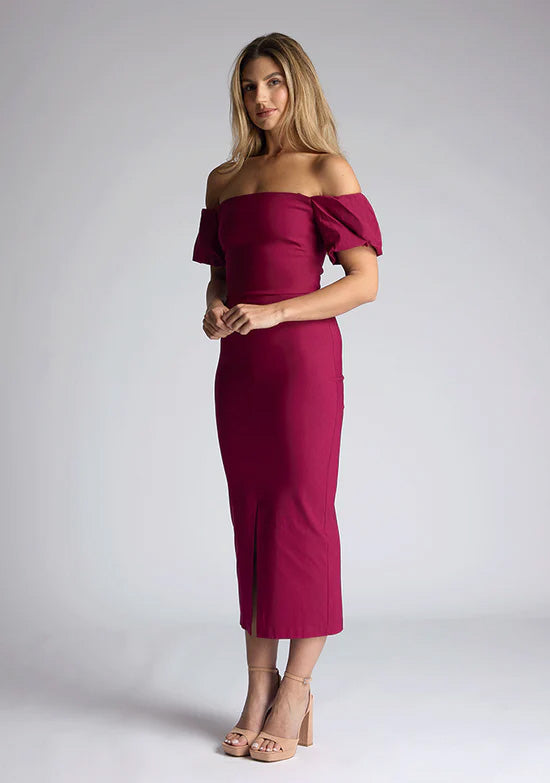 Front quarter image of a blonde model wearing a berry midaxi dress with a bardot neckline gracefully frame off shoulders, while the back zip ensures a seamless silhouette. The dress features is the Vesper Quinton Berry Midaxi Dress