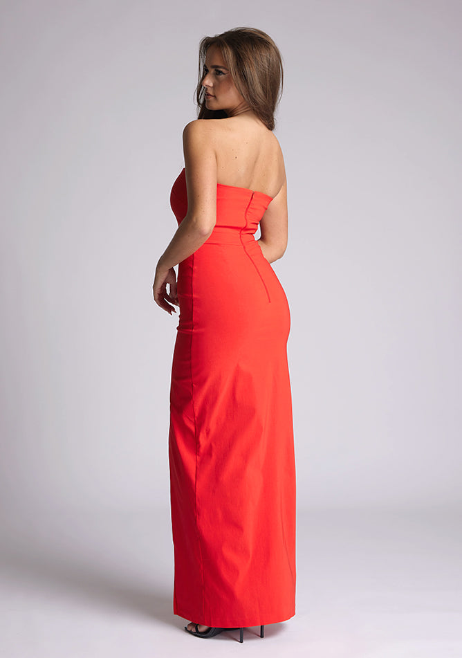 Back quarter image of the model wearing a red bodycon maxi dress, with a strapless neckline and a front split. The design featured is the  Vesper Salma Red Midaxi Dress.