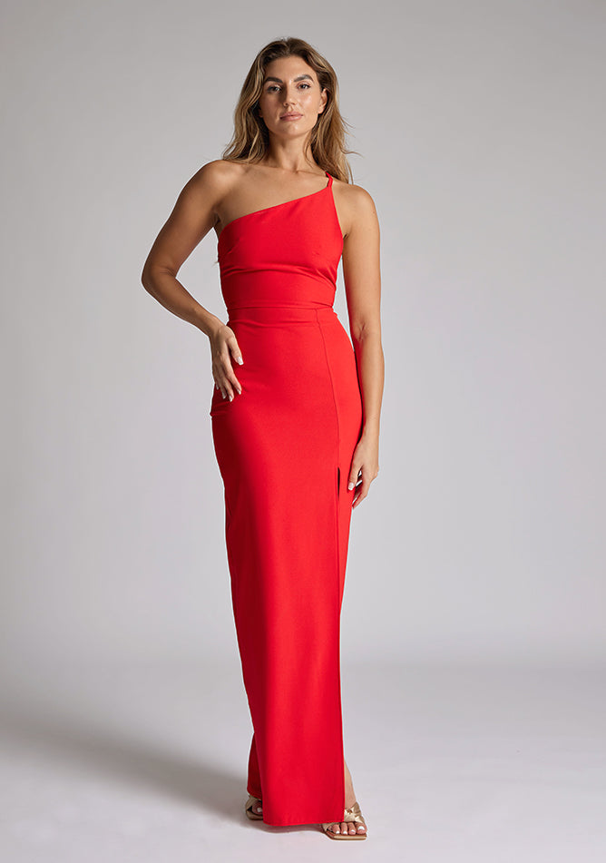 Front image of a model wearing a red maxi dress with a asymmetric neckline, one shoulder strap, front skirt split and open back with asymmetric strap across back. The design featured is Vesper Viva Red Maxi Dress