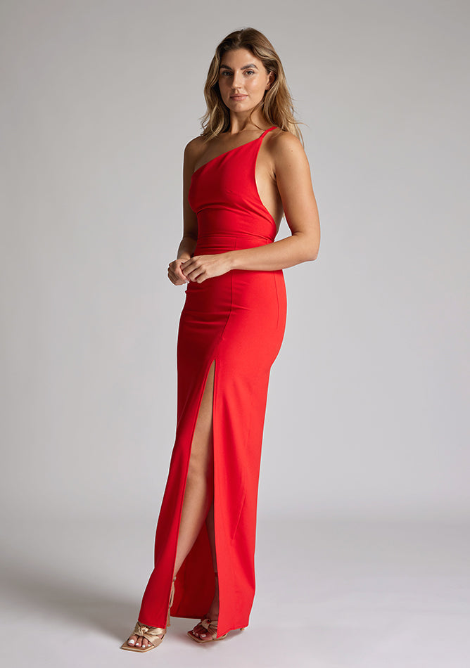 Front quarter image of a model wearing a red maxi dress with a asymmetric neckline, one shoulder strap, front skirt split and open back with asymmetric strap across back. The design featured is Vesper Viva Red Maxi Dress