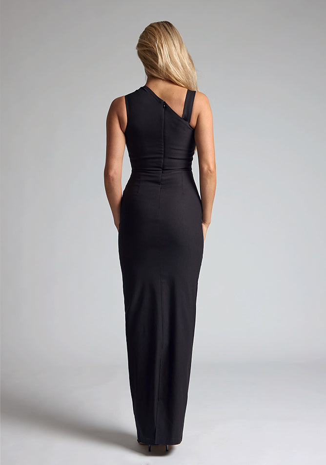Back image of a blonde model wearing a black maxi dress with an sleeveless silhouette and add a modern twist. The design features is the Vesper Wyatt Black Asymmetric Maxi Dress