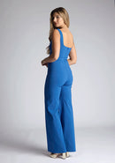 Back quarter image of a model wearing a petrol blue jumpsuit, featuring a square neck, wide leg and sleeveless design. The design featured  is the Vesper Alana Petrol Blue Wide Leg Jumpsuit