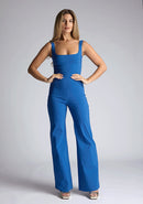 Front image of a model wearing a petrol blue jumpsuit, featuring a square neck, wide leg and sleeveless design. The design featured  is the Vesper Alana Petrol Blue Wide Leg Jumpsuit