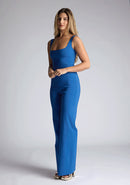 Front image of a model wearing a petrol blue jumpsuit, featuring a square neck, wide leg and sleeveless design. The design featured  is the Vesper Alana Petrol Blue Wide Leg Jumpsuit