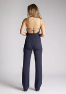 Back image of a model wearing a backless navy halter neck jumpsuit, featuring a key hole cut out and straps which cross at the back. The design featured is the Vesper Amanda navy jumpsuit