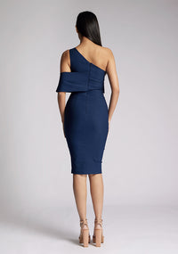 Back image of a model wearing a navy midi dress, featuring an asymmetric neckline, one shoulder detail and statement band around one arm. The dress featured is the Vesper Amos Navy Midi Dress.