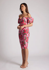 Quarter front image of a model wearing a floral bardot dress, featuring puff sleeves and a midi length. The dress featured is the Anastasia Pink Floral Bardot Midi Dress