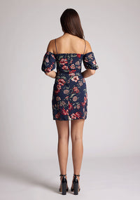 Back image of a model wearing a navy floral dress with thin straps and off the shoulder sleeves. The dress featured is the Anisa navy floral mini dress
