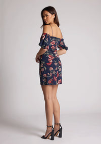 Quarter back image of a model wearing a navy floral dress with thin straps and off the shoulder sleeves. The dress featured is the Anisa navy floral mini dress