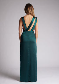 Back image of a model wearing a pine satin cowl neck dress, the dress is maxi length and features back detailing with the straps. The dress featured is the Anoushka pine maxi dress