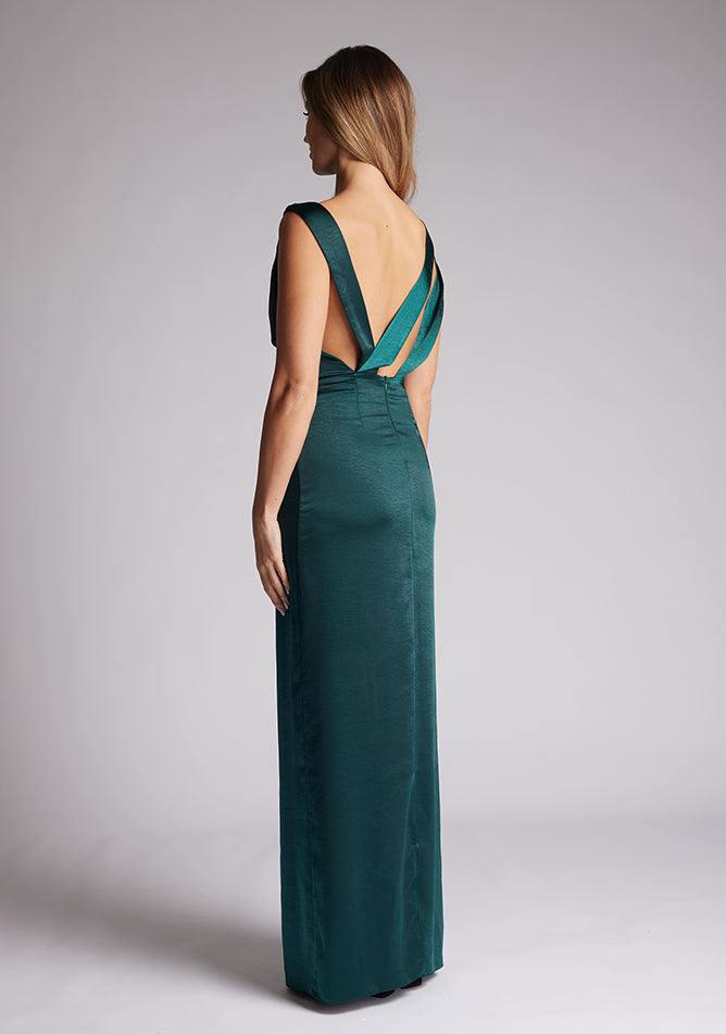 Back quarter image of a model wearing a pine satin cowl neck dress, the dress is maxi length and features back detailing with the straps. The dress featured is the Anoushka pine maxi dress
