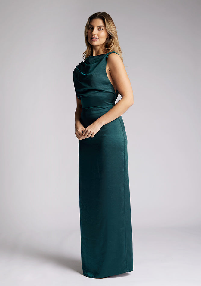 Front quarter image of a model wearing a pine satin cowl neck dress, the dress is maxi length and features back detailing with the straps. The dress featured is the Anoushka pine maxi dress