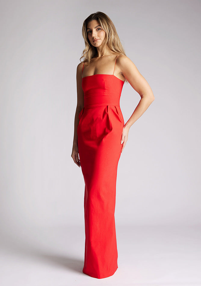 Front quarter image of a model wearing a red square neck maxi dress, featuring delicate straps and waist detailing. The dress featured is the Vesper Bergen maxi dress