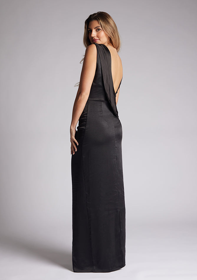Back quarter image of a model wearing a black satin maxi dress, featuring a cowl neck ruched detail and an open back. The dress featured is the Vesper Bertie black maxi dress