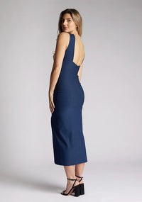 Back quarter image of a model wearing a navy cut out midaxi dress. The dress features a key hole cut out at the front and a back less design. The dress featured is the Vesper Carter navy midaxi dress