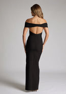 Back image of model wearing a black maxi dress with a off-shoulder design for a sophisticated touch, a front skirt split adds a subtle allure. The design featured is the Vesper Delta Black Maxi Dress