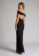 Back quarter image of model wearing a black maxi dress with a off-shoulder design for a sophisticated touch, a front skirt split adds a subtle allure. The design featured is the Vesper Delta Black Maxi Dress