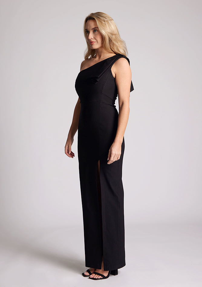Front quarter image of a model wearing a black one shoulder maxi dress with bow detailing at the shoulder. The dress featured is the Eimer black maxi dress