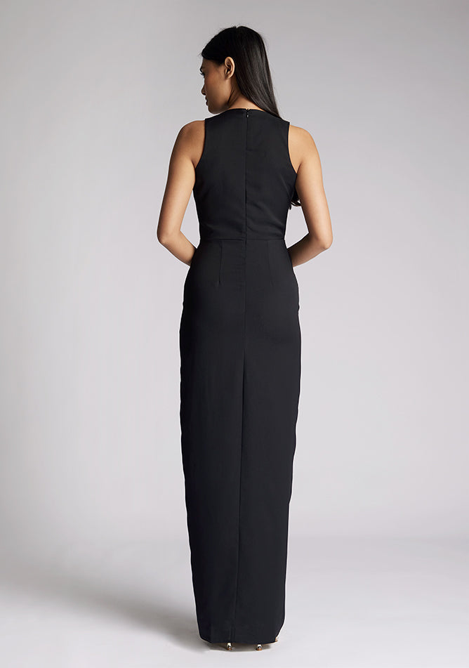 Back image of a model wearing a black sleeveless maxi dress, featuring a front split and a v neck design. The dress featured is the Vesper Elba black maxi dress