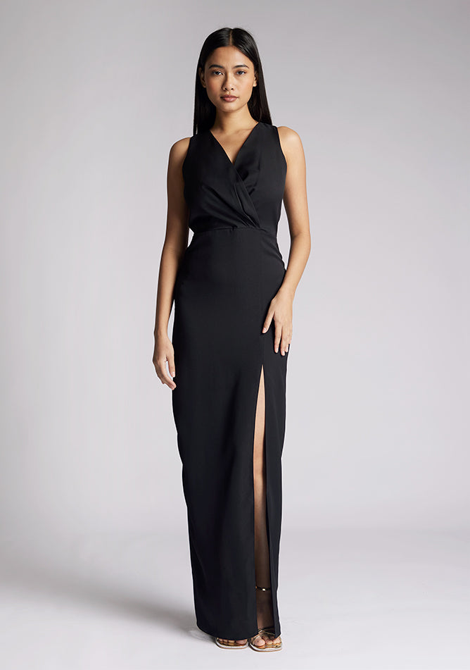 Front image of a model wearing a black sleeveless maxi dress, featuring a front split and a v neck design. The dress featured is the Vesper Elba black maxi dress