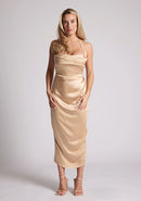 Front image of a model wearing a champagne satin midaxi dress featuring a halter neck and a ruched design. The dress featured is the Vesper Electra champagne satin midaxi dress