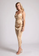 Front quarter image of a model wearing a champagne satin midaxi dress featuring a halter neck and a ruched design. The dress featured is the Vesper Electra champagne satin midaxi dress