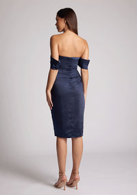 Back quarter image of a model wearing a navy satin midi dress, featuring a pleated panel across the front and two arm bands. The dress featured is the Vesper Fleur navy midi dress