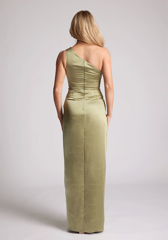 Back image of a model wearing an olive satin dress in a maxi length. This dress features a one shoulder detail and asymmetric neckline with a band across the neckline and front skirt split. The dress featured is Vesper Fliss olive maxi dress
