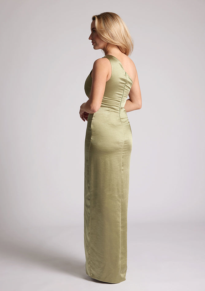 Back quarter image of a model wearing an olive satin dress in a maxi length. This dress features a one shoulder detail and asymmetric neckline with a band across the neckline and front skirt split. The dress featured is Vesper Fliss olive maxi dress