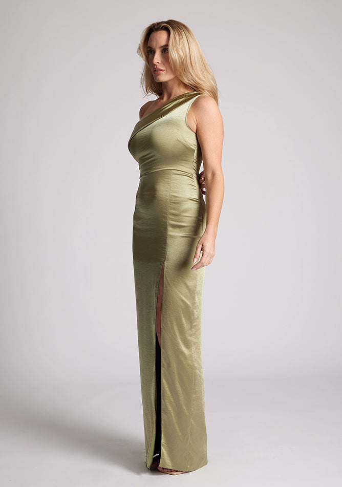 Front quarter image of a model wearing an olive satin dress in a maxi length. This dress features a one shoulder detail and asymmetric neckline with a band across the neckline and front skirt split. The dress featured is Vesper Fliss olive maxi dress