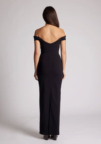 Back image of a model wearing a black maxi dress, featuring off the shoulder short sleeves and a dipped back design. The dress featured is the Vesper Holland black maxi dress